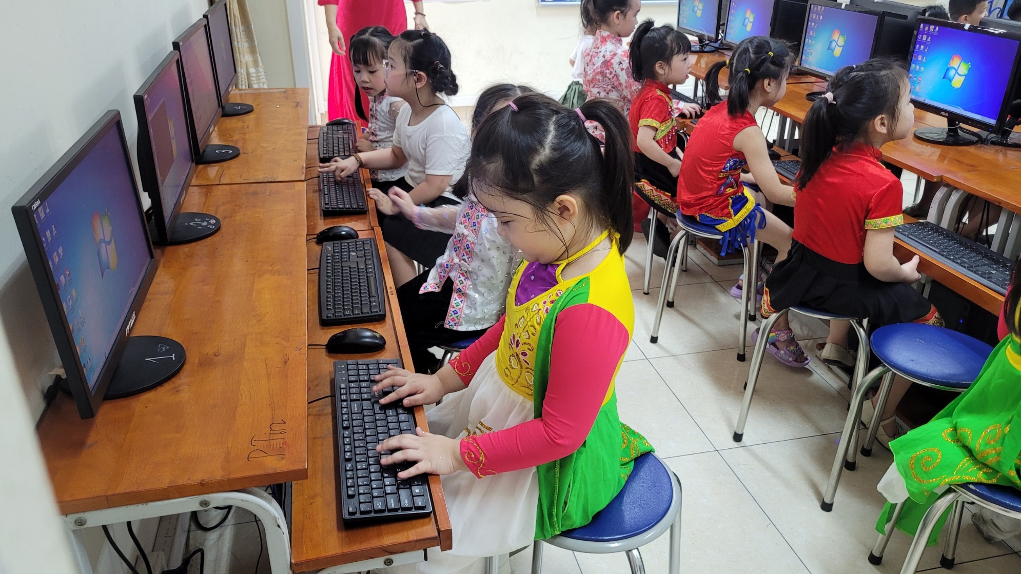 A group of children sitting at a desk using computers

Description automatically generated